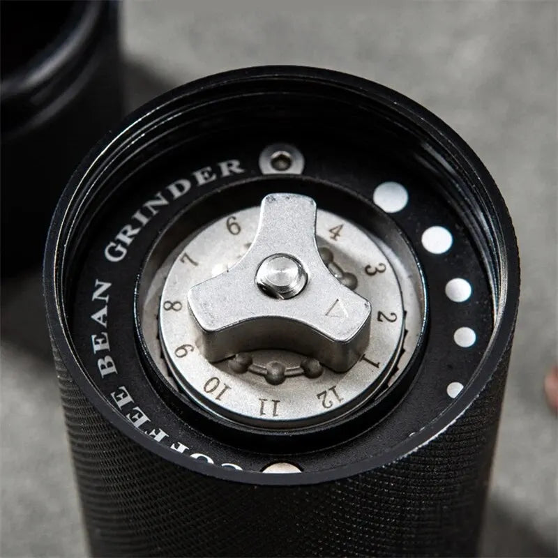 Close-up of a black coffee grinder with a metallic adjustment wheel on a gray surface.